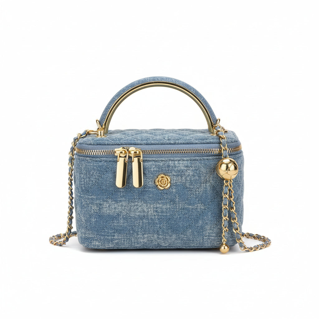 Denim handbag with gold accents held by a person, with a blurred background