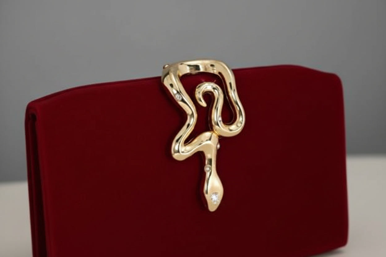 Red clutch with gold snake-shaped clasp on a gray background, featuring the brand 'Opulaura'.